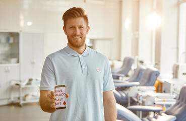 Minimal waist up portrait of smiling man holding smartphone with Give blood save life slogan at blood donation center, copy space
