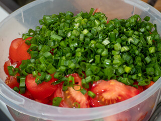 Chopped green onions and tomatoes in a cup.