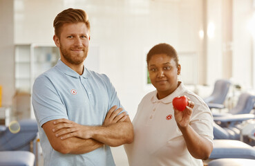 Minimal waist up portrait of smiling blood donors holding red heart to camera at blood donation...