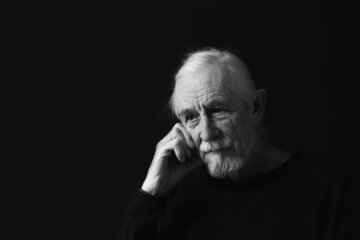 Low key studio black and white portrait of sad beautiful gray hair old man. 
