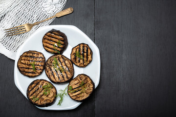 Grilled eggplants in plate on black wood background.