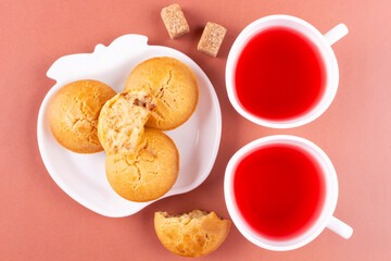 Homemade rice muffins on a saucer and raspberry tea in cups on a pink (coral) background. Rice flour cupcakes. Breakfast with a gluten-free diet.