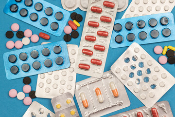 A pile of pills in blister packs. Blister packs full of multi-colored pills. Close-up on a blue background. Full colored pills package. Pharmaceutical blister pack. Pack of pills with tablets.