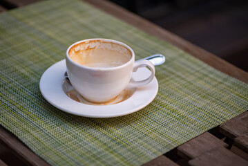 Empty coffee cup with milk foam stains and light lipstick imprint on the edges leaved on table of outdoor cafe