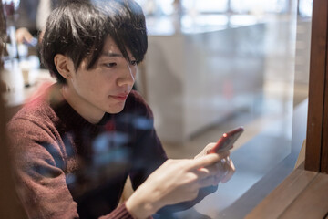 カフェの窓辺でスマートフォンを操作する20代男性