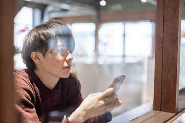 カフェの窓辺でスマートフォンを操作する20代男性