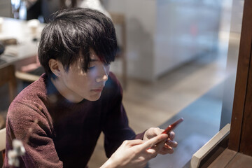 カフェの窓辺でスマートフォンを操作する20代男性
