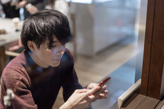 カフェの窓辺でスマートフォンを操作する20代男性