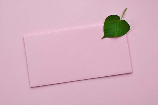 Mockup of  pink paper card with green leave in the shape of a heart on pink background closeup. Valentine's Day, wedding, Mother's Day greeting card 