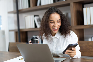 Smile business woman working with laptop computer, using mobile phone and holding black coffee on...