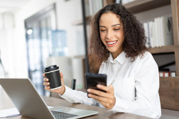 Smile business woman working with laptop computer, using mobile phone and holding black coffee on hand in the office.