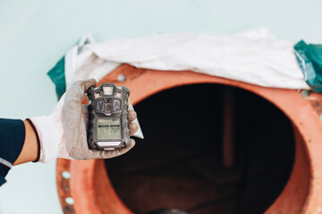 Worker hand holding gas detector inspection safety gas testing at front manhole tank