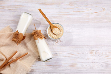 Sesame milk in bottles, sesame seeds in a jar on a wooden background. A healthy vegetarian and vegan drink, a plant-based milk substitute. Zero waste.
