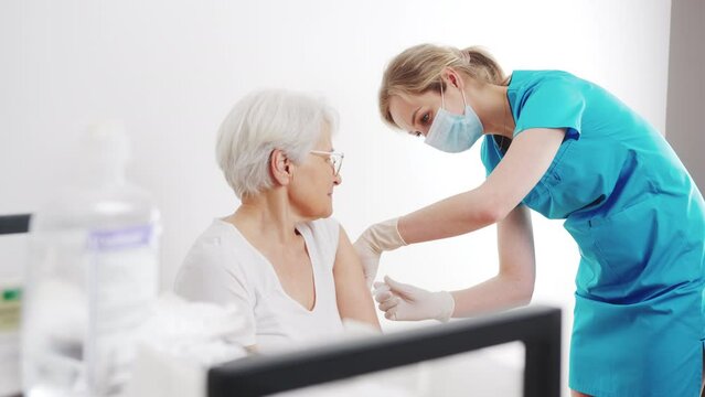 young attractive blond Caucasian nurse making vaccine injection to senior female patient medium shot hospital healthcare concept. High quality 4k footage