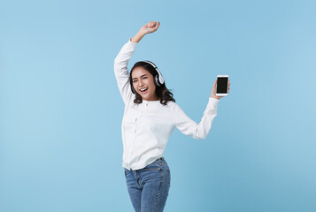 Happy beautiful Asian teen woman listening music on mobile phone wear headphones and dance on blue background.
