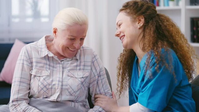 Friendly nurse and senior woman sincerely laughing, talking and having fun