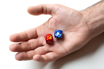 On the man's palm are two dice with images of the symbols of the hammer and sickle and white star. The concept of the confrontation between the two ideologies of communism and capitalism. - obrazy, fototapety, plakaty