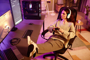 High angle view of young adult Caucasian woman playing shooter video game using console in living...