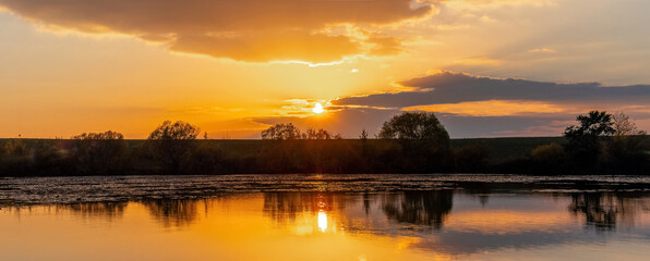 Obraz premium Sunrise or sunset on the river. Reflection of the sky and clouds in the river water