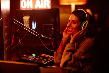 Modern young adult woman working on radio broadcast in amateur home studio at night turning on her...