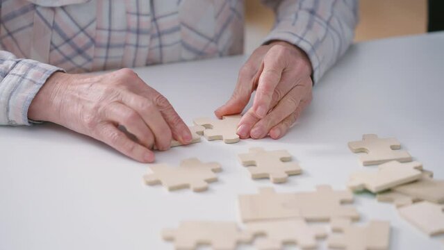 Elderly woman connecting jigsaw puzzle pieces, exercising mind and motor skills