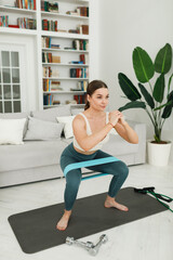 Fototapeta na wymiar Active young woman doing morning exercises squatting alone in the living room, serious girl in sportswear doing squat muscle training at home for body healthy lifestyle concept