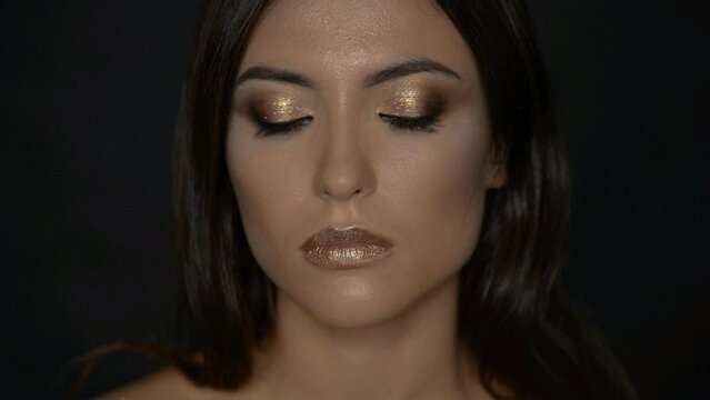 Young woman with golden makeup. She looks into the camera.