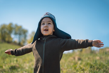Girl with outstretched arms in pilot suit plays outdoors.