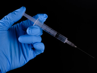 A man is wear gloves and hold a syringe. Isolated with black background. Vaccination and medical concept.