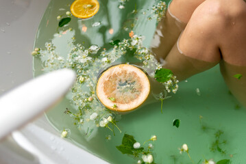 Woman taking a bath with flowers and oranges, close-up, top view.