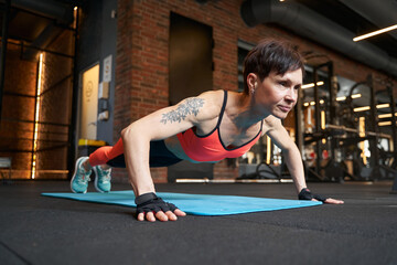Fototapeta premium Muscular woman performing push-up on gym floor