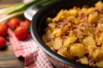 Stewed pork with potatoes and onions on a brown wood.Composition with cherry tomatoes and green onions.Space for copy. Place for text. Recipe for fried potatoes.