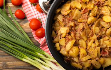 Stewed pork with potatoes and onions on a brown wood.Composition with cherry tomatoes and green onions.Space for copy. Place for text. Recipe for fried potatoes.