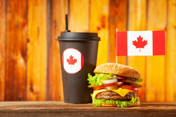 Close-up home made beef burger with Canada flag on the top and black paper cup on wooden table over...