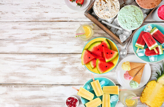 Cool summer foods side border. Assorted ice cream, popsicles and fruit. Top view over a white wood background.