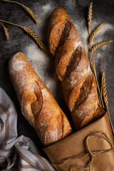 French baguette, long loaf with
wheat ears on black background with flour on the table