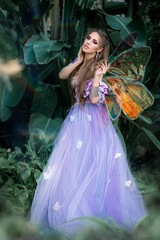 A beautiful woman is a little cute fairy with butterfly wings in a green exotic forest. Fantasy...