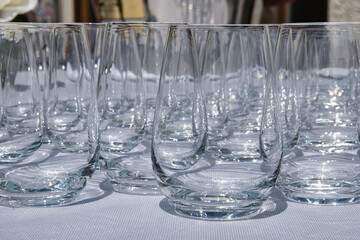 Perfectly lined up glasses sitting on a table with white table cloths, on a sunny day, being ready to be used by the party guest/ wedding guests. 