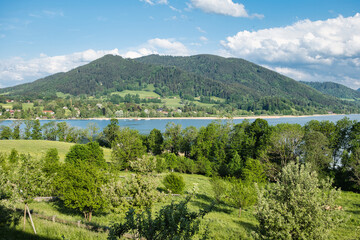 Landscape shot of Lake Tegernsee, Bavaria, Germany on a sunny day with some clouds in the background of a small hill. 