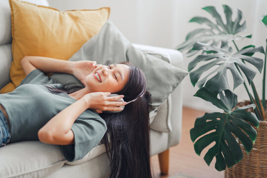Happy woman relaxing in her sofa at home, Smiling girl is listening to music with headphones and lying down with eyes closed, Enjoy good quality sound, Stress free concept.