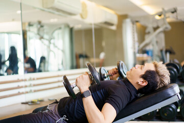 Fototapeta na wymiar Active Asian sportsman doing a weight exercise in a gym - fitness by lifting up a dumbbell.