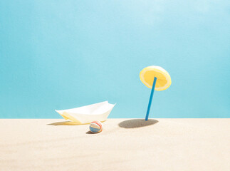 Sunshade, parasol made of lemon and blue drinking straw. Beach ball and boat in the sand. Minimal...