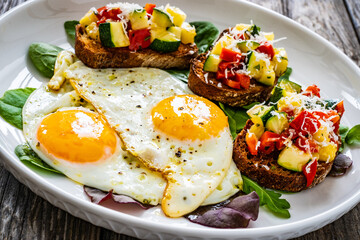Sunny side up eggs, bruschetta and fresh vegetables on wooden table
