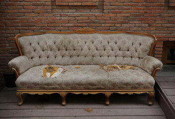 A very old ripped couch.  An old broken brown sofa needs repair. Large holes, springs, synthetic...