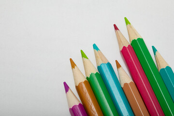 close up of vivid coloured pencils entering the bottom of the frame on a white background copy space from above