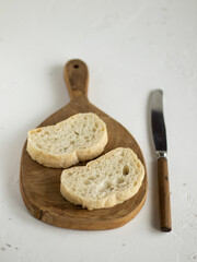 Two pieces of ciabatta on the wooden board and knife near. Piece of italian bread. White background, copy space