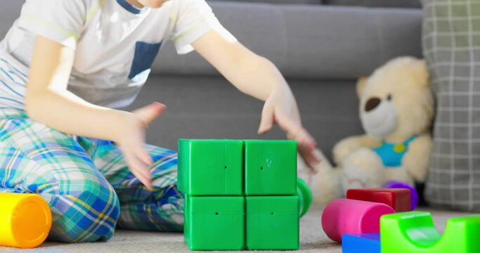 A child is playing with children building blocks on floor. Building a tower of cubes. Educational toys for children