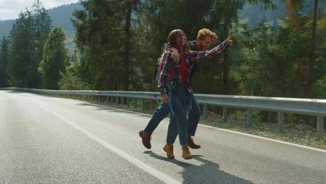 Hipsters hiking having fun on mountains hitchhike. Tourists walking highway road