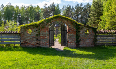 Stone wall, wooden gate, entrance to the Bible Garden. Spring in the garden. An old brick wall overgrown with plants