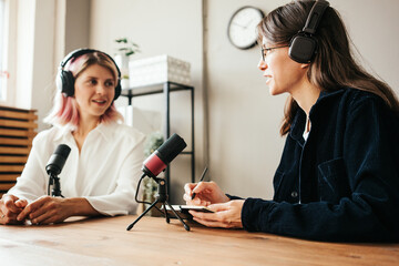 Two woman hosts in local broadcat studio recording audio podcast, interesting conversation
